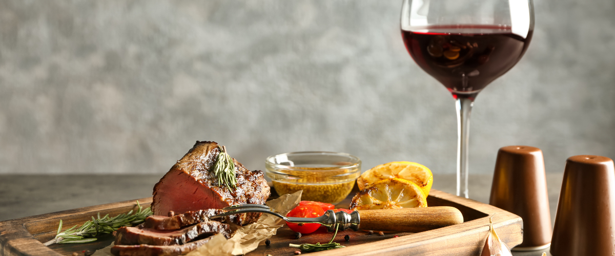 A glass of red wine beside a steak on a board
